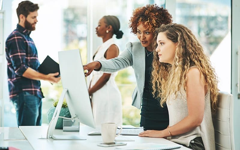 Femme senior au bureau aide jeune femme devant ordinateur